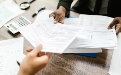 Picture of tax documents being passed between two people over a desk. Picture compliments of RDNE Stock Project at Pexels.com